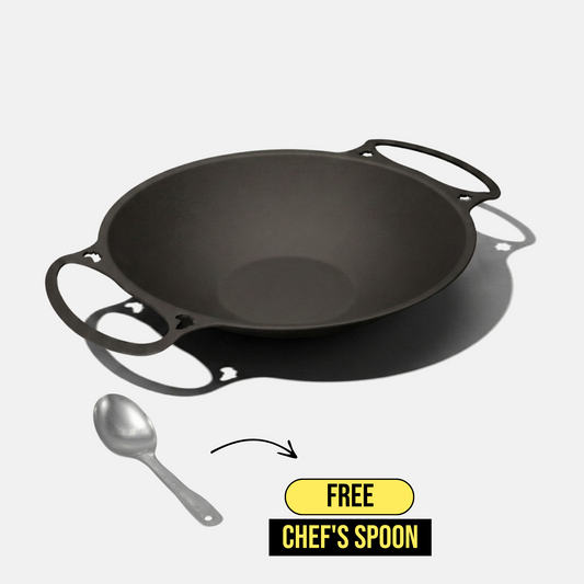 A black iron kadhai pan with loop handles, shown on a light gray background with a chef's spoon and a promotional badge that says 'FREE CHEF'S SPOON'.