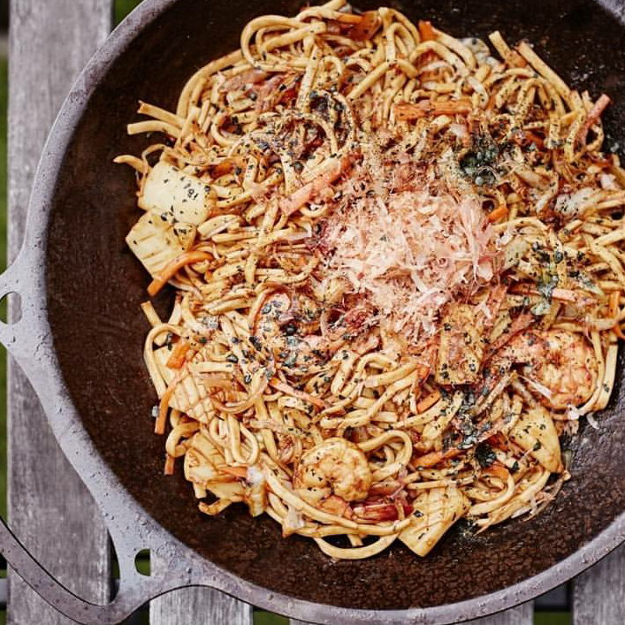 Overhead view of a cast iron skillet filled with pasta and shrimp on a weathered wooden table.