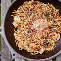 Overhead view of a cast iron skillet filled with pasta and shrimp on a weathered wooden table.