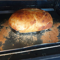 A freshly baked sourdough bread loaf resting on a dark baking tray with scattered cinnamon inside an oven.